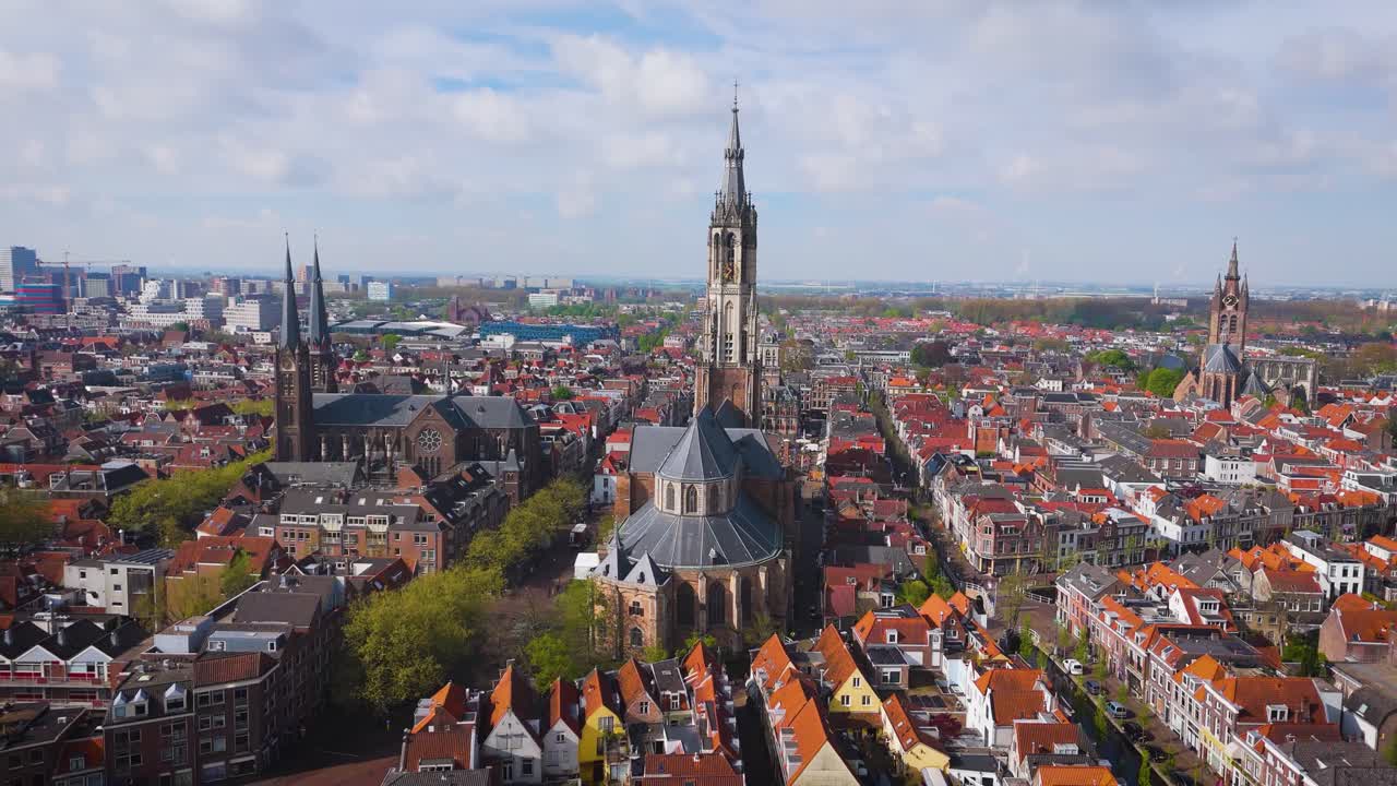 Elevated drone view of the towering Nieuwe Kerk in Delft, dominating the red-roofed cityscape below. Captures the blend of medieval Dutch charm and modern skyline surroundings.