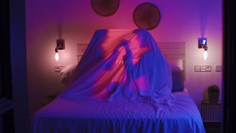 close-up shot of a couple holding hands under a lit up sheet on a bed