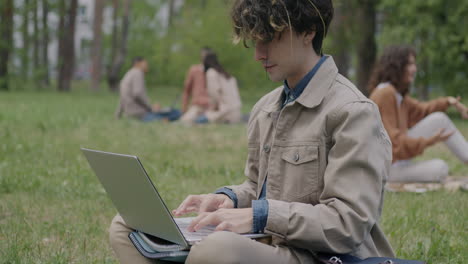 young person working on laptop in park with friends