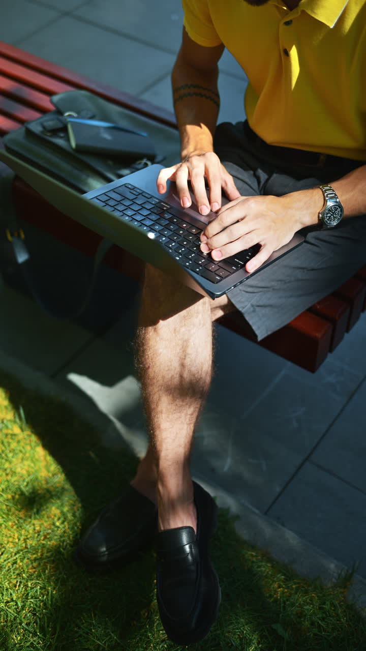 Man in yellow shirt talking standing on a bench and working on a laptop. Vertical