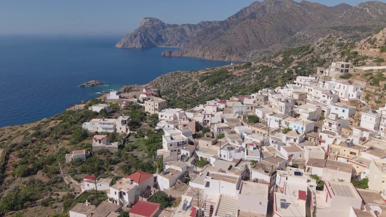 Drohnenaufnahme von oben vom Dorf Mesochori auf Karpathos, die seine traditionelle Anordnung und die zerklüftete Insellandschaft, die sich über die umliegenden Berge erstreckt, enthüllt.