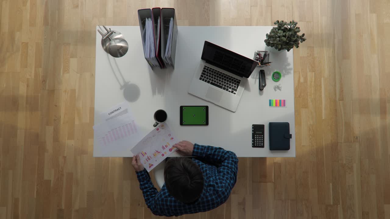 Top view shot of an office worker sitting on desk using tablet with greenscreen chroma key drinking coffe with floating sun