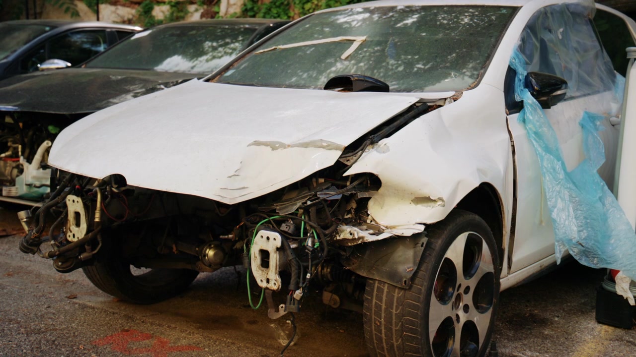 Auto bianca gravemente danneggiata con paraurti anteriore mancante e parti meccaniche esposte parcheggiata in uno sfasciacarrozze