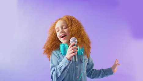 foto de estúdio de uma menina usando fones de ouvido cantando karaokê em um microfone contra um fundo roxo