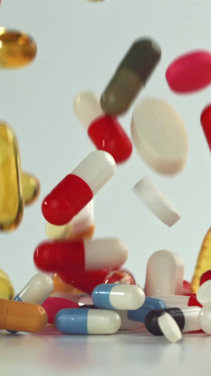 Colorful Pills and Capsules Falling in Slow Motion on White Background