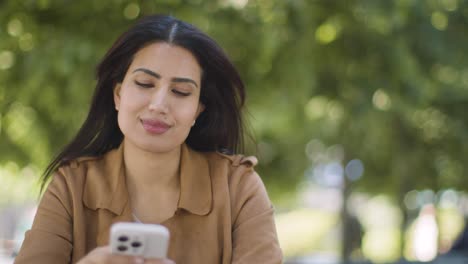 muslim woman sitting at outdoor table on city street looking at mobile phone