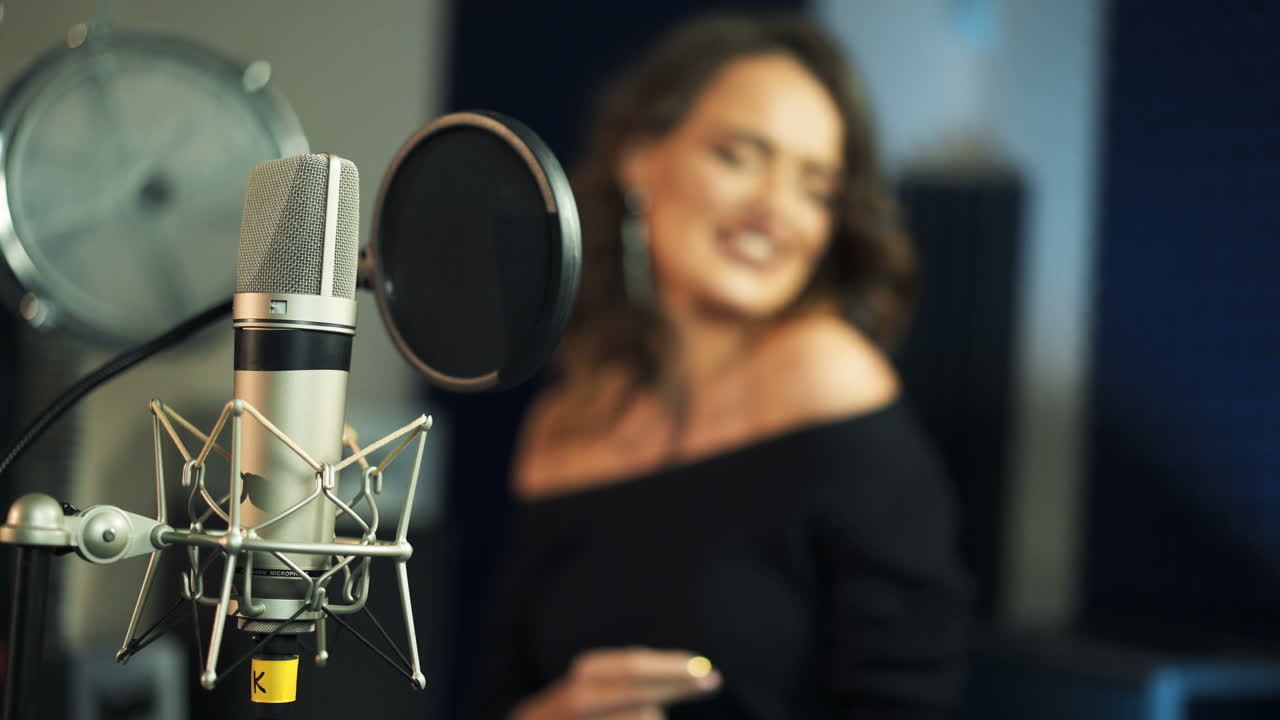 Professional condenser studio black microphone on blurred background of a woman singing. Musical equipment and a woman singer in studio