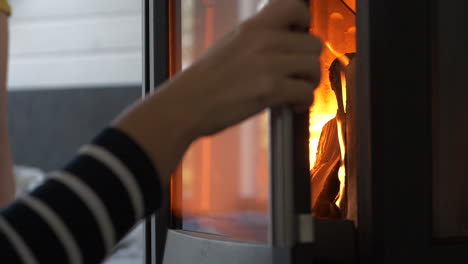 Woman-hand-closes-glass-door-of-wood-stove