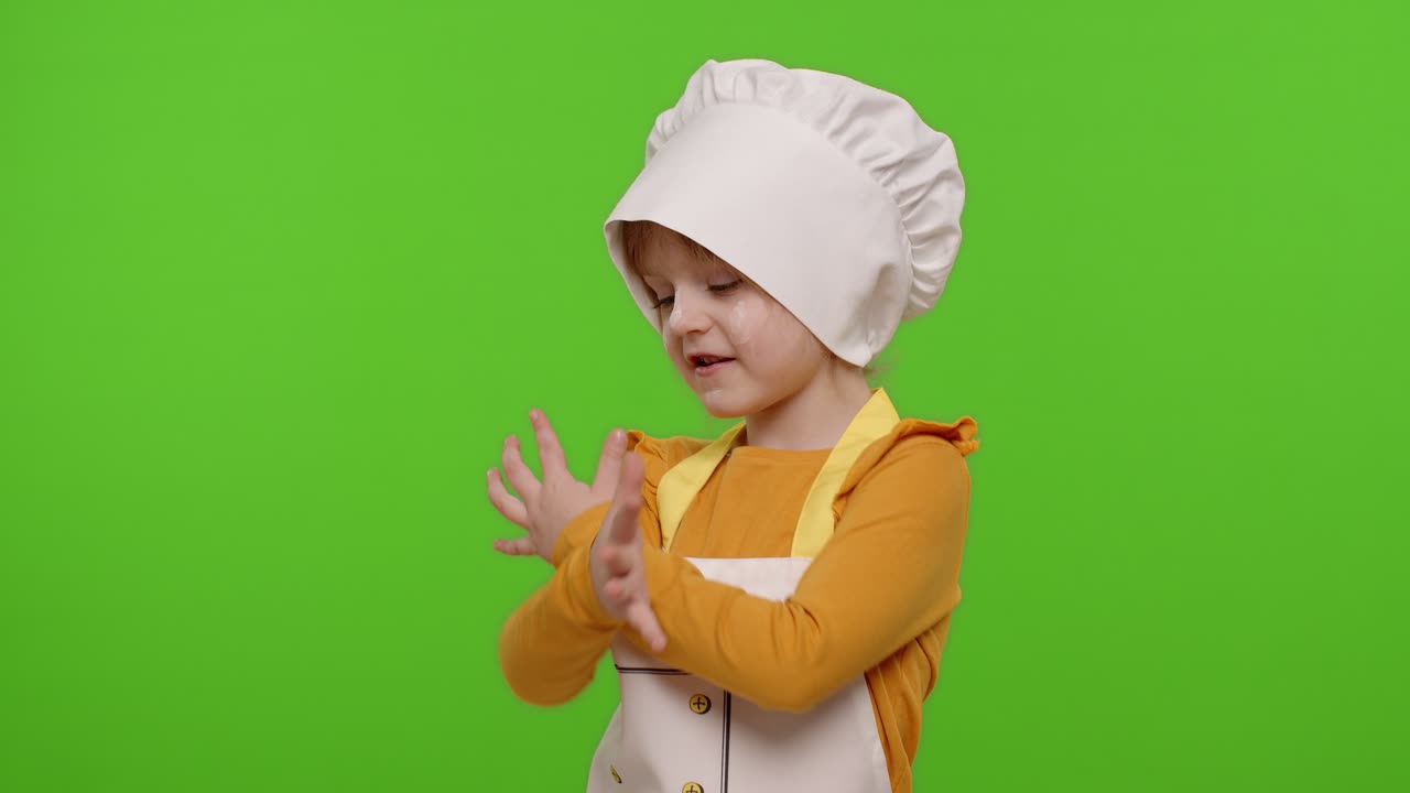 Bambina divertente vestita da cuoca/chef/fornaia con grembiule e cappello che balla, scherza e fa smorfie