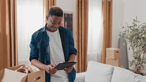 a young boy hangs out in his new apartment, unpacking cardboard boxes left over from the move, browsing the web on tablet, social media, laughing at memes, browsing inspiration