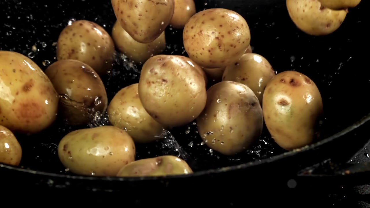 Patate fresche che cadono e schizzano in una padella nera