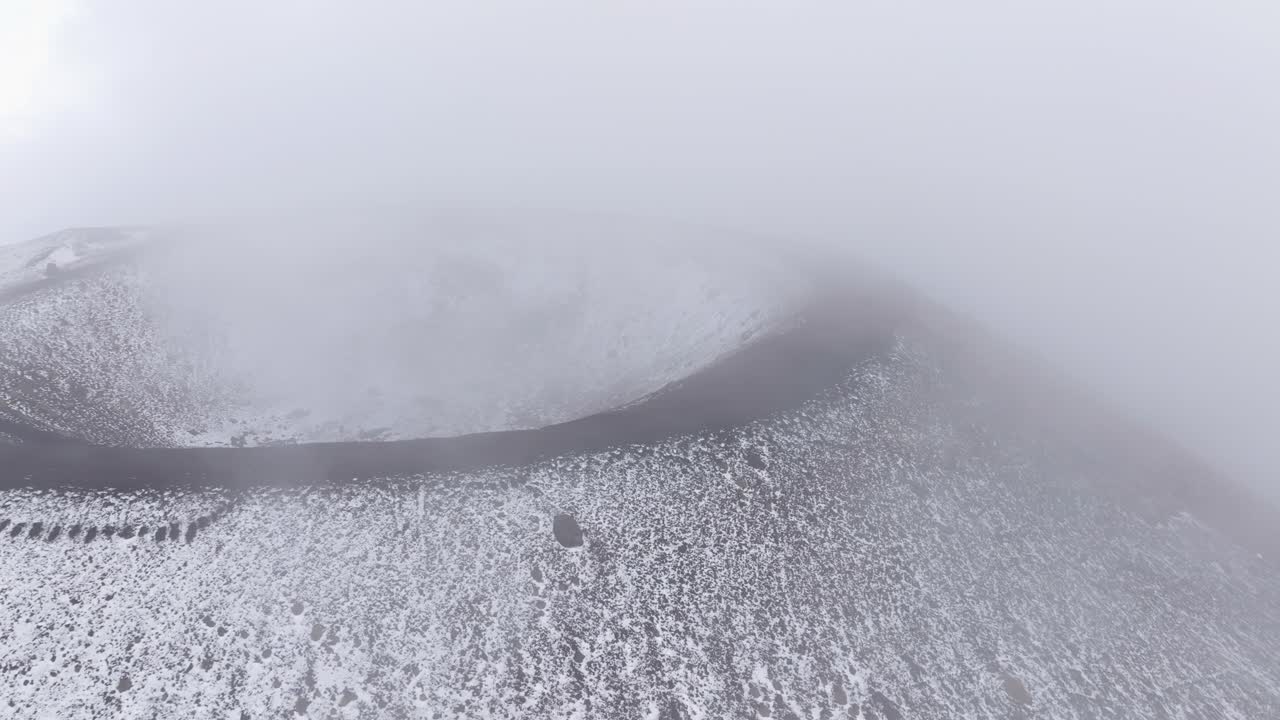 An aerial shot of one of Mount Etna's extinct craters, with the cone of the crater clearly visible. Dense fog surrounds the area.