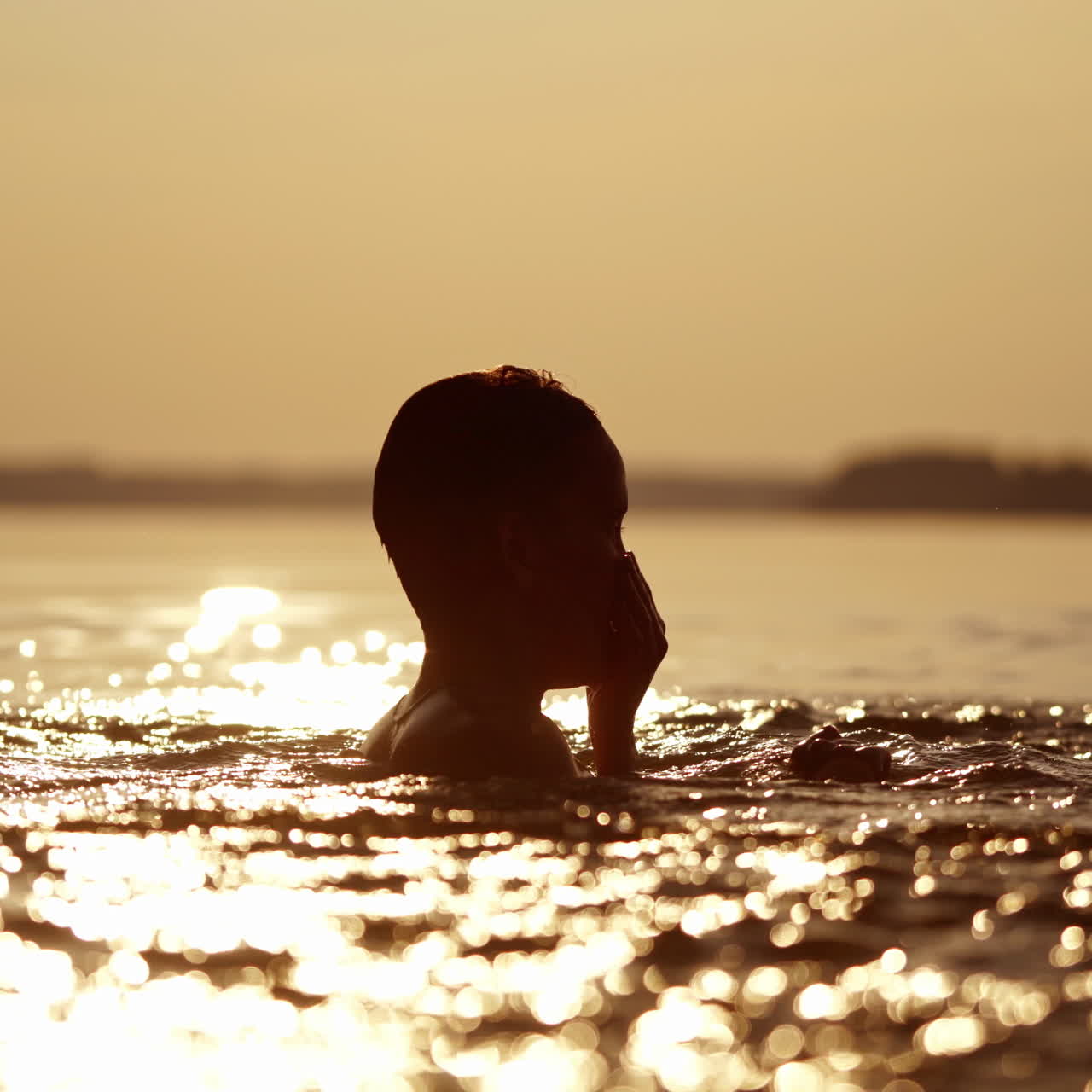 Silhouette of two cute boys in water background. Children swimming in the river in the evening at sunset.