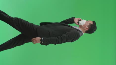 side view of asian business man talking on mobile phone while walking on green screen chroma key, wear medical mask