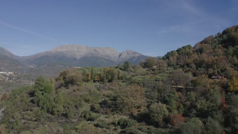 rising-flight-with-surprise-effect-in-a-valley-discovering-a-rural-environment-with-a-population-and-amazing-mountains-on-a-hillside-with-colorful-trees-in-autumn-and-a-road-with-cars-Avila-Spain