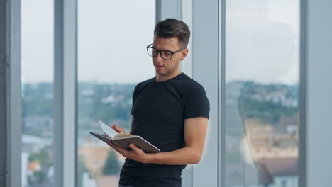 confident young millennial male in glasses looking through the paper notebook. man turns his head looking aside.