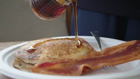 pouring warm maple syrup on a short stack of pancakes for a traditional american breakfast - slow motion