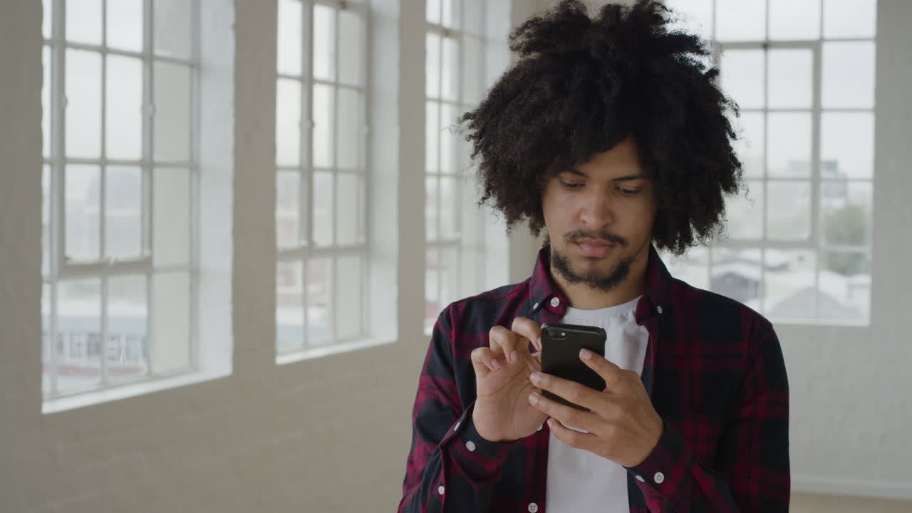 ritratto di un giovane studente di razza mista che usa uno smartphone, invia messaggi, naviga online, social media, invia messaggi sulla tecnologia dei telefoni cellulari nell'appartamento
