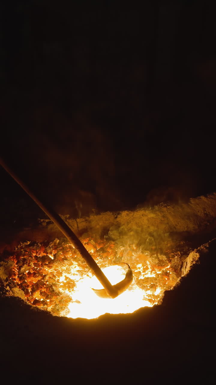 Foundry worker stirring bright molten metal in a dark smelting furnace