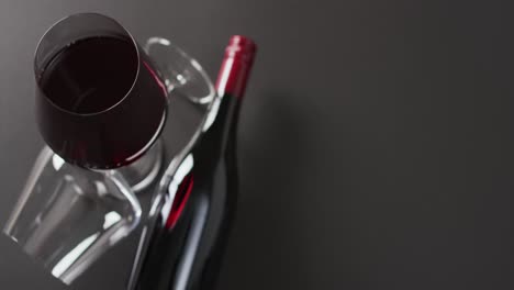 glass of red wine and red wine bottle lying on grey surface with copy space