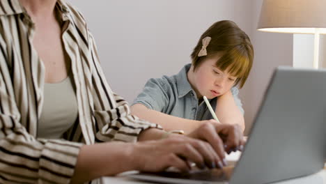 closeup of woman working on laptop and her daughter doing homework next to her