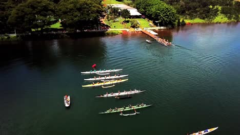 Vista-Aérea-Sobre-Los-Equipos-De-Remo-Del-Malecón-A-Orillas-Del-Lago-Que-Se-Preparan-Para-Las-Carreras-De-Deportes-Acuáticos-Del-Lago