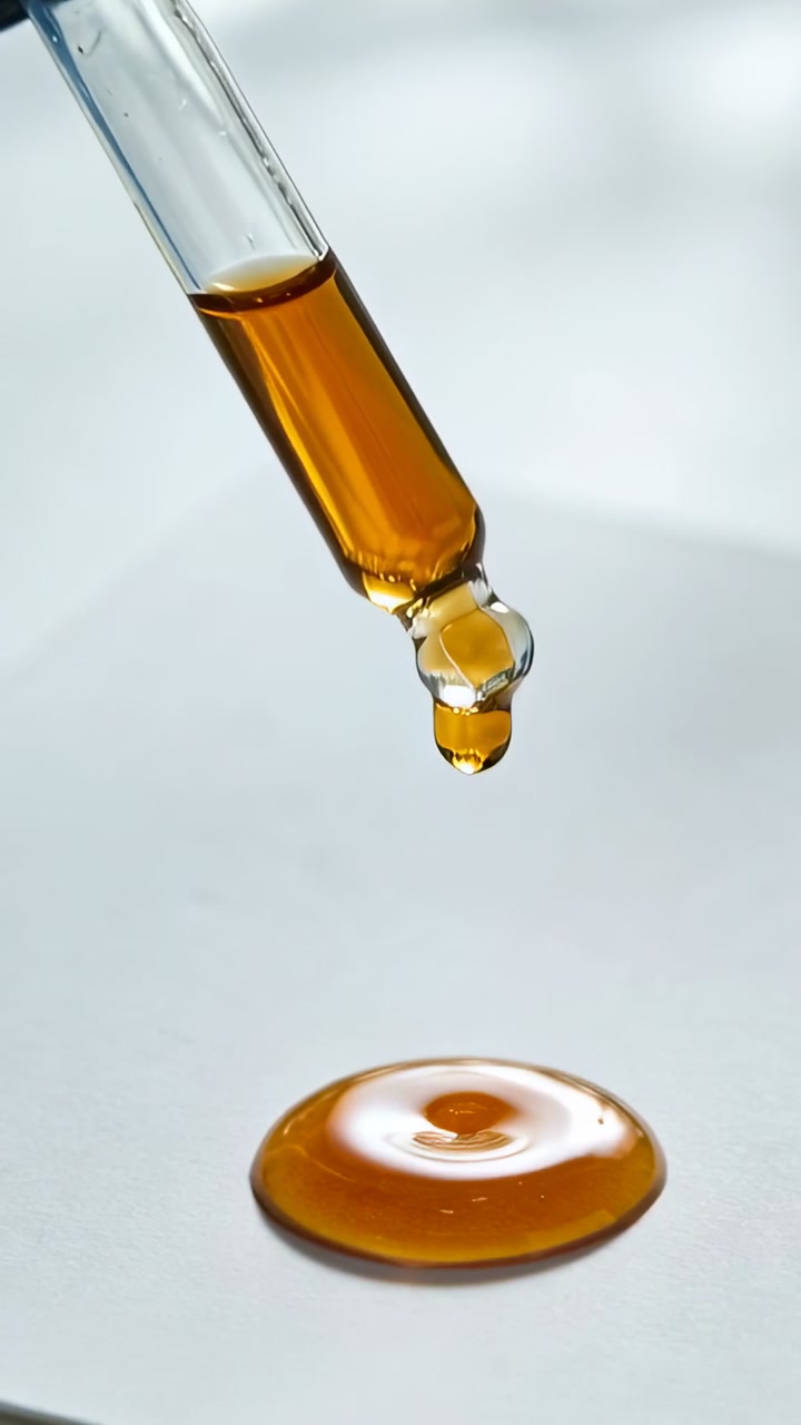 Vertical video: Glass dropper forming bead, releasing droplet onto puddle, showing beauty texture