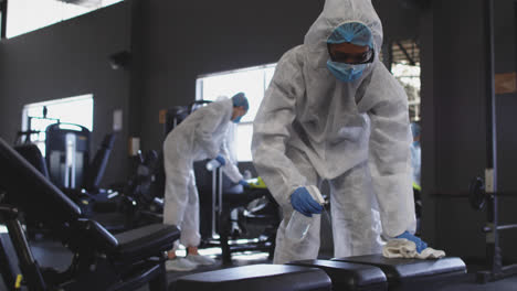 team of health workers wearing protective clothes cleaning gym by using disinfectant sprayer