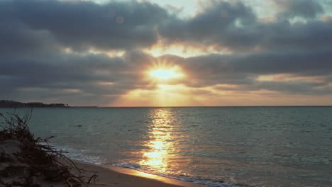 At-Zorritos-Beach-in-Tumbes,-Peru,-the-sun-is-setting-in-the-horizon-as-the-water-of-the-sea-washes-up-at-the-shore