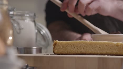 primer plano del hombre en la cocina de casa agregando relleno de chocolate al pastel recién horneado en la superficie de trabajo