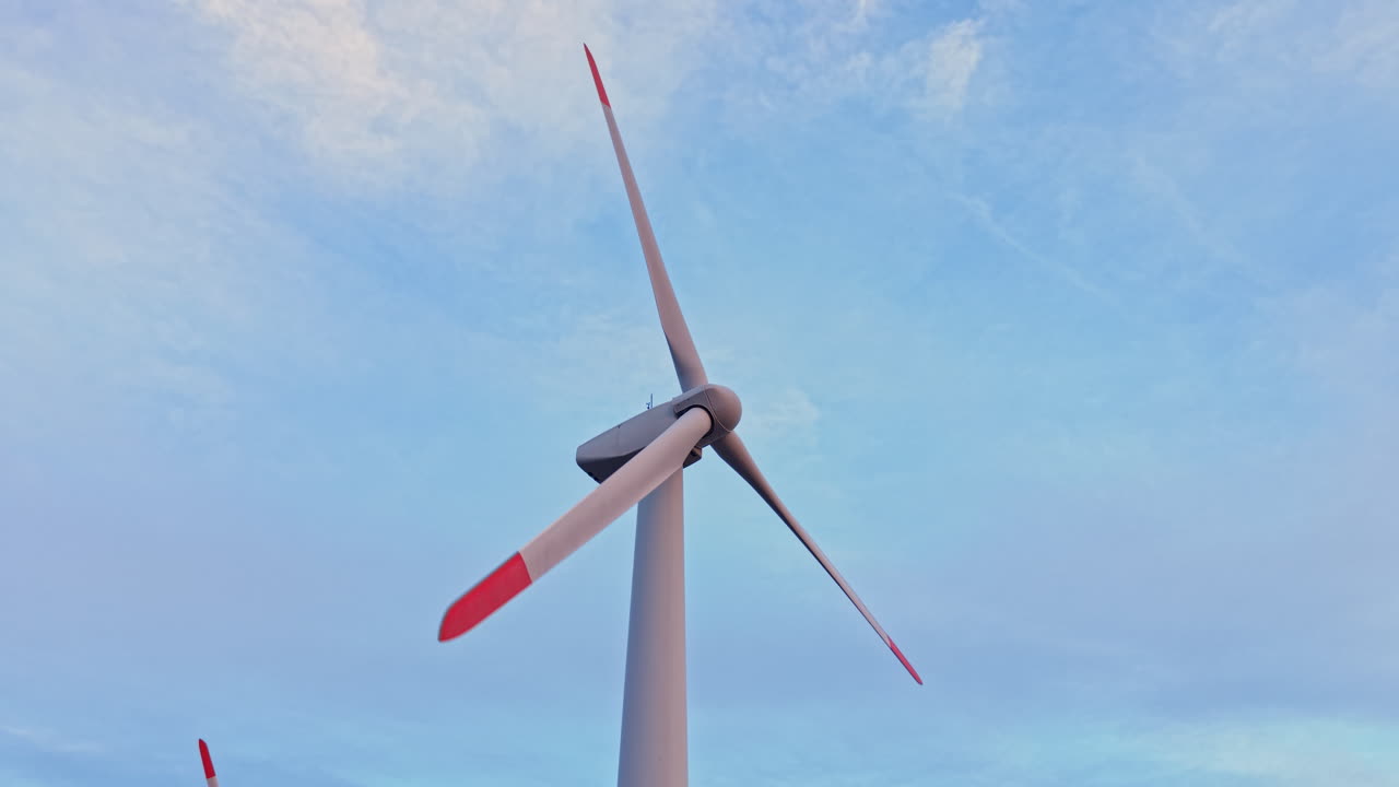 Una turbina eolica ruota contro un cielo limpido in una giornata di sole in una zona rurale, catturando il vento per la produzione di energia e la sostenibilità.