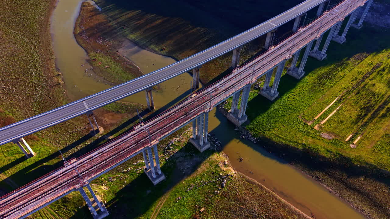 Perspektif ketinggian dua jembatan beton paralel, satu untuk mobil dan satu untuk kereta api, yang ditopang oleh pilar-pilar tinggi di atas sungai. Pemandangan sudut tinggi jembatan layang jalan raya dan kereta api.