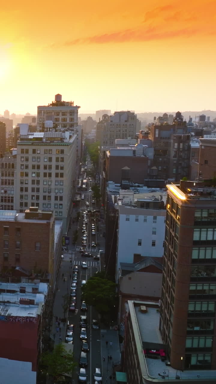 Setting sun over the multi-storied buildings of New York. Drone rising over a busy street of metropolis. Orange sky backdrop. Vertical video