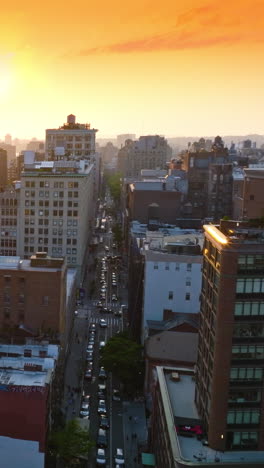 setting sun over the multi-storied buildings of new york. drone rising over a busy street of metropolis. orange sky backdrop. vertical video
