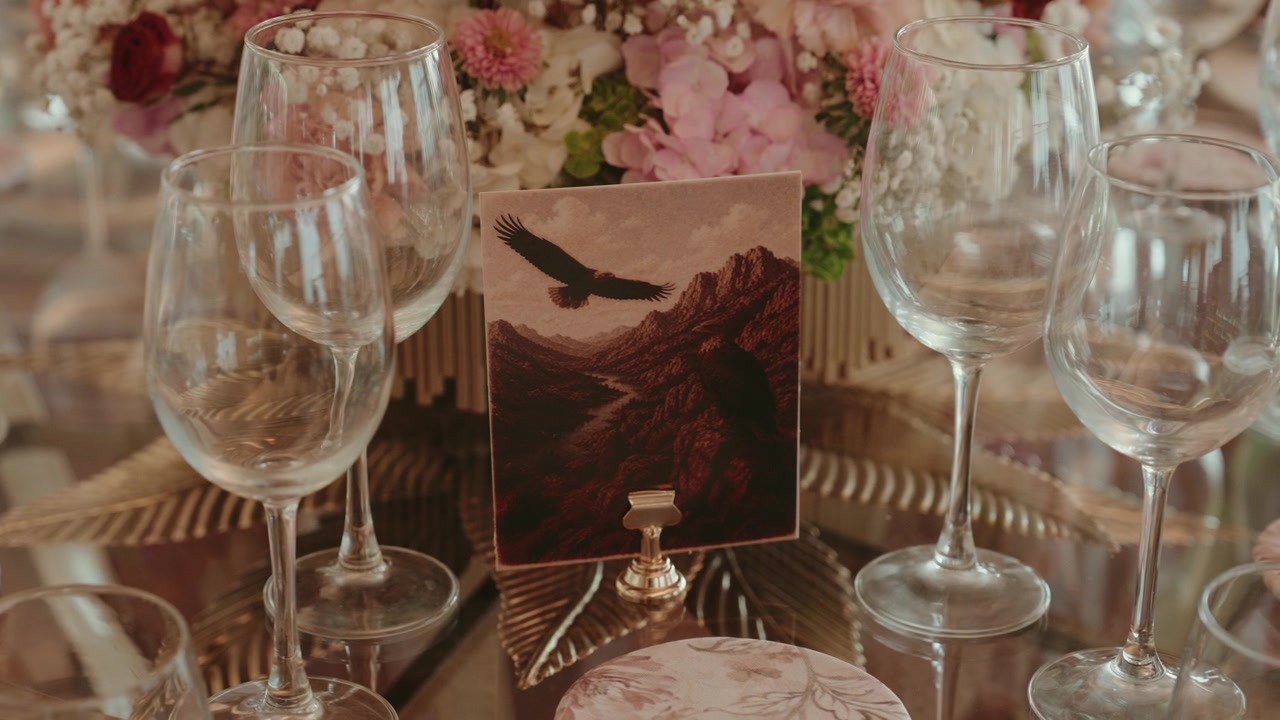 Elegant table setting for an event, featuring wine glasses and a table number card with a flying eagle over mountains