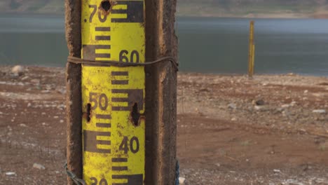 tilting up shot of an old rusty water level gauge post on the water edge with view of lake, mountain range, and blue sky at a national park