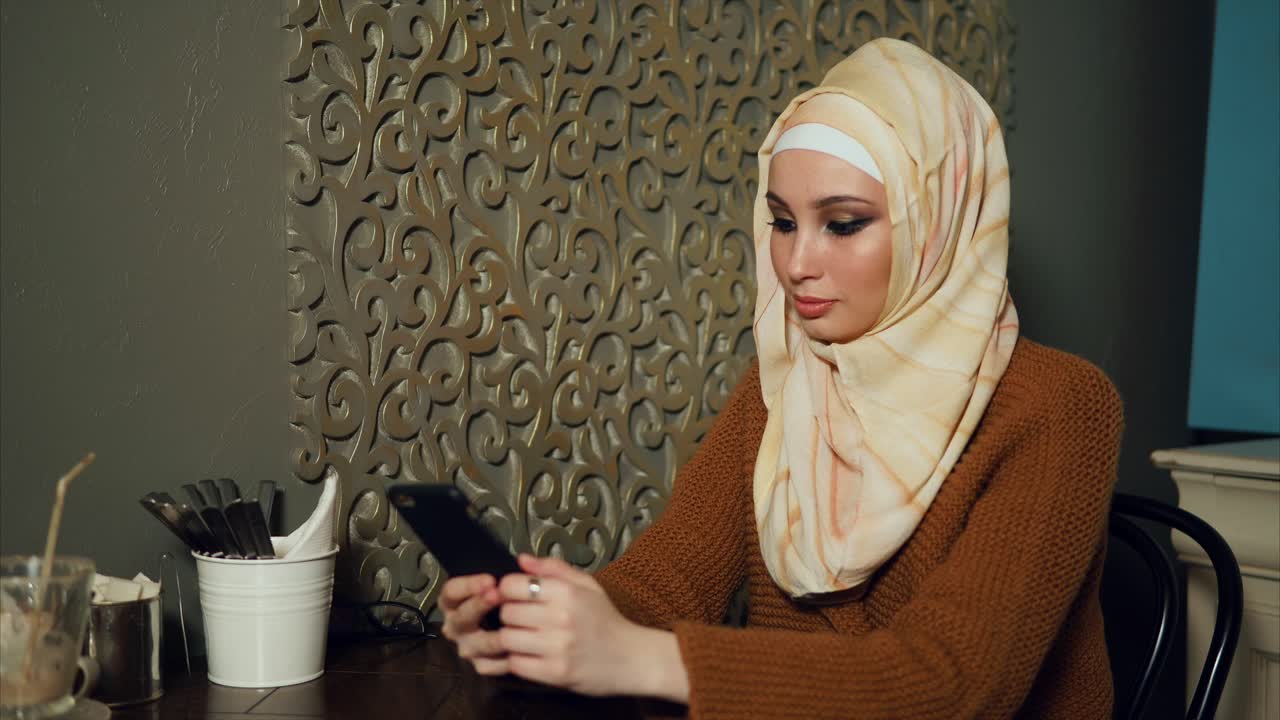 Young Muslim woman using smartphone in a cafe
