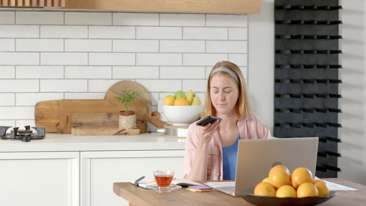 Working from home, woman using laptop and talking on phone in kitchen, copy space