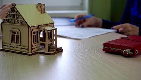 la mujer firma el contrato. el agente de bienes raíces pasa los papeles. luego da las llaves. hay una casa de madera en la mesa, las llaves de la propiedad