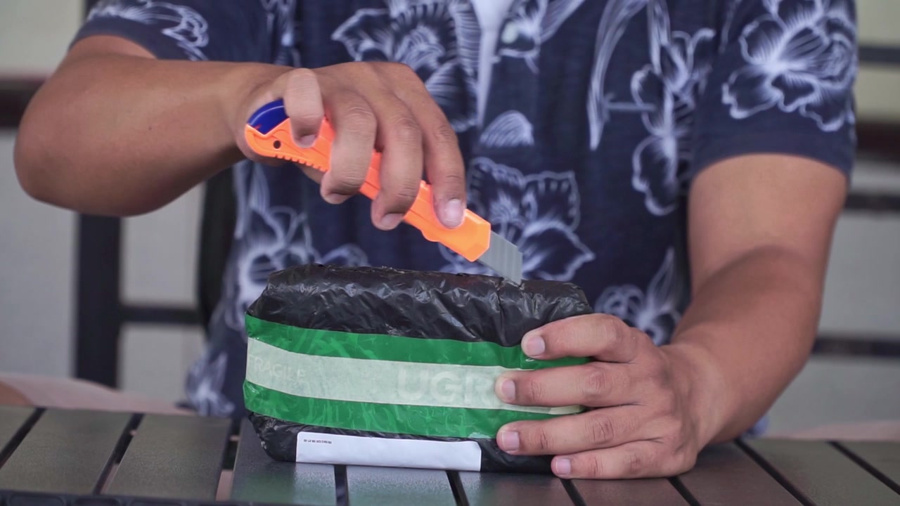Unboxing paket dengan pisau cutter, menampilkan pengiriman belanja online, pembukaan paket, layanan kurir, dan konsep pengalaman konsumen.