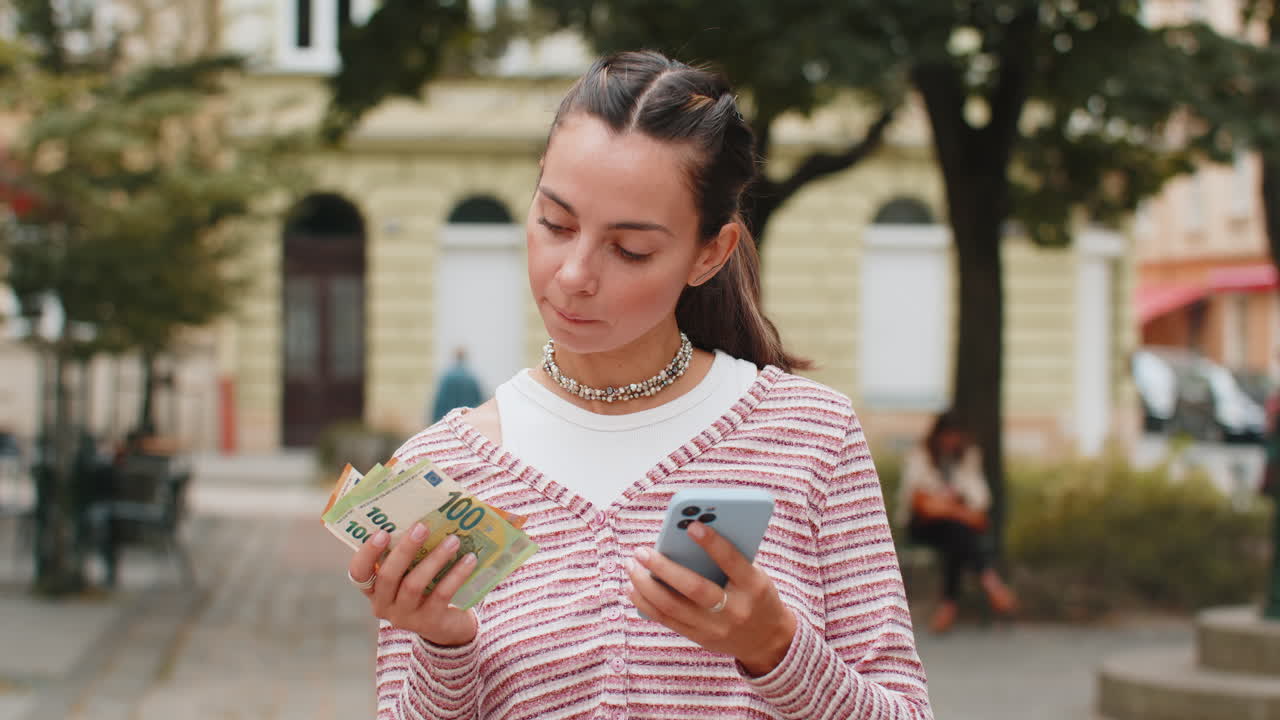 Donna felice che conta i soldi in euro con l'app di calcolatrice per smartphone in una strada urbana