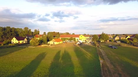 Vuelo-De-Drones-Aéreos-Más-Tranquilo-Volar-Hacia-Adelante-Tiro-De-Drones-Desde-Una-Granja-Con-Largas-Sombras-De-árboles-Al-Atardecer-De-Verano-En-Un-Lago-En-Un-Pequeño-Pueblo-En-Brandeburgo-Alemania