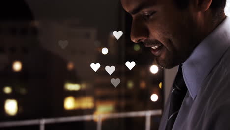 smiling man holding phone with heart icons and city lights in background