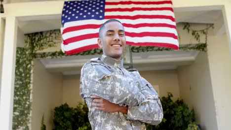 Portrait-of-happy-biracial-male-soldier-in-garden-over-american-flag