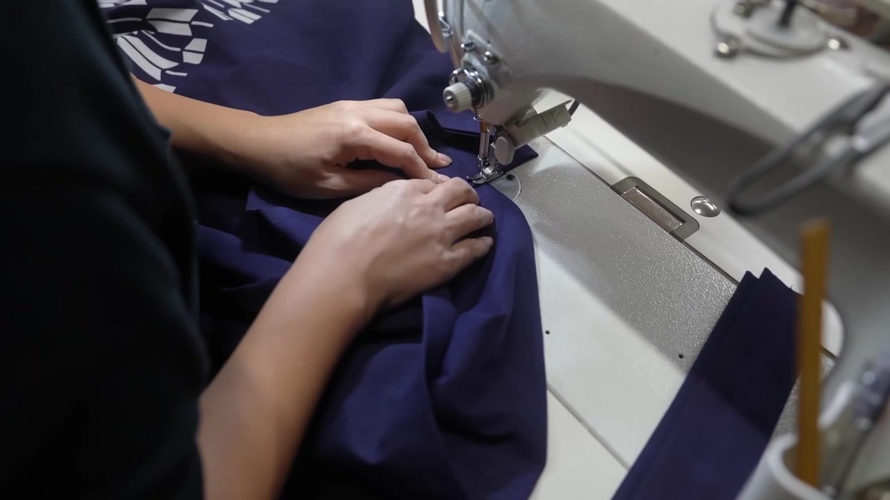 Close view of hands positioning navy cloth at the needle plate of an industrial sewing machine with scissors resting alongside