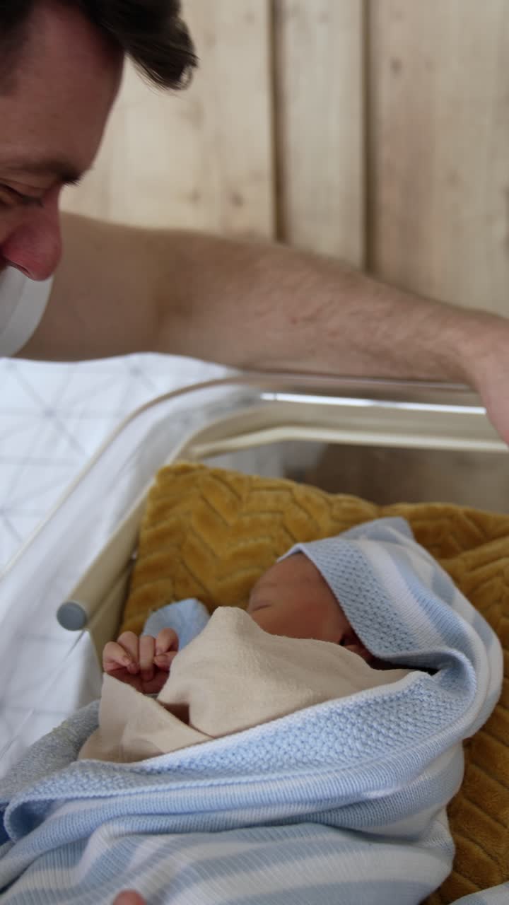 Papà felice e sorridente accanto alla culla con il suo neonato. Genitore e bambino dopo il parto in ospedale. Video verticale.