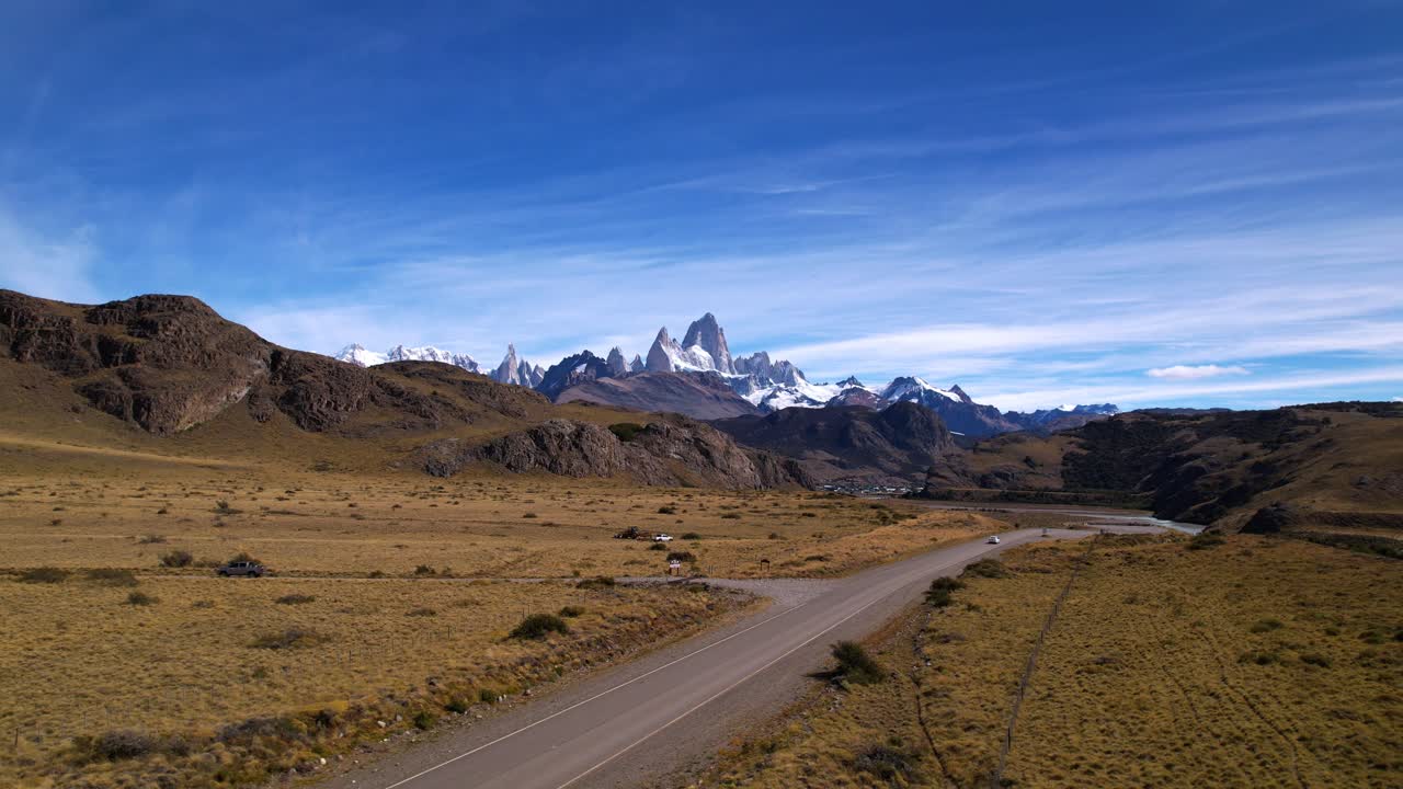 Aerial Drone Footage Showcases The Breathtaking Fitz Roy Mountain In Argentina, Revealing A Snowy Peak And A White Car Driving Along The Road By The Las Vueltas River On A Sunny Summer Day.