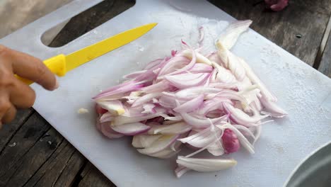 Cerrar-Picar-Cebollas,-Manos-Femeninas-Cortar-Cebollas-Con-Cuchillo-Amarillo-En-Pizarra-Blanca