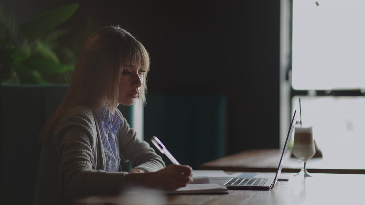 An Asian woman student writes an online lecture on campus with a pen. Sitting in the library a Korean woman student listens to a lecture
