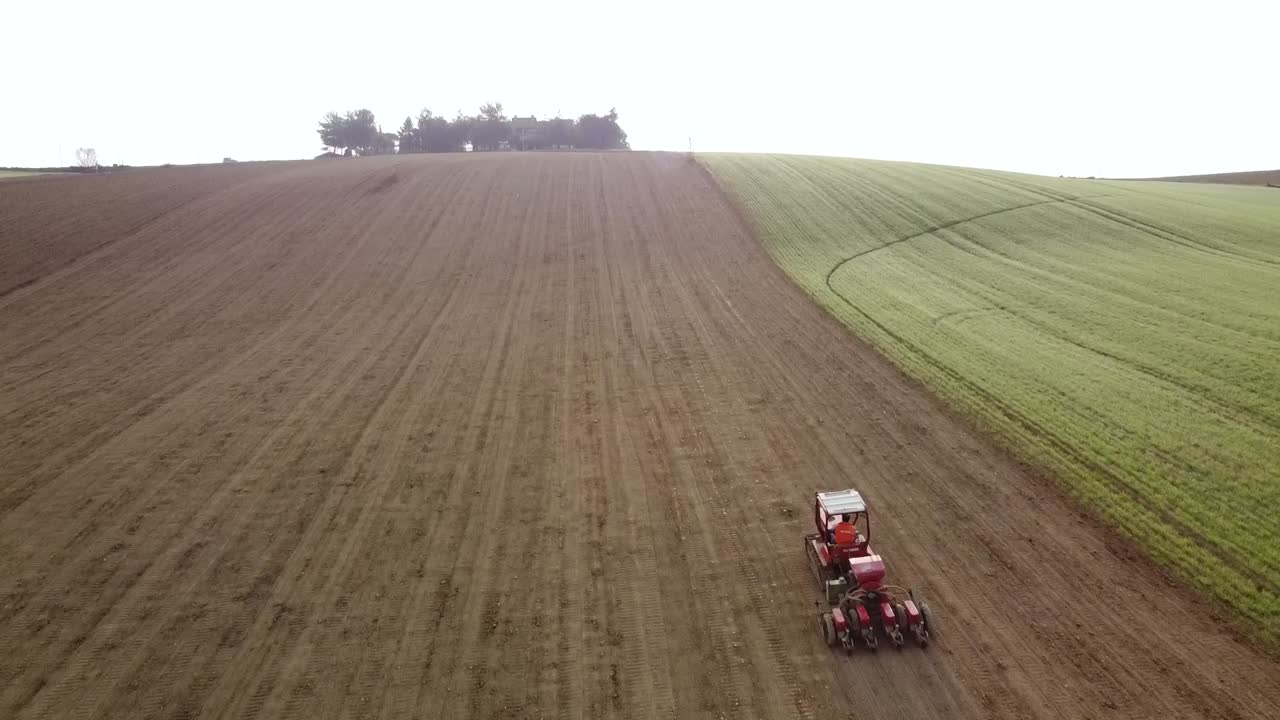 Aerial scenic agricultural land farm landscape with red tractor driving uphill plowing and preparing with modern equipment before the seeding